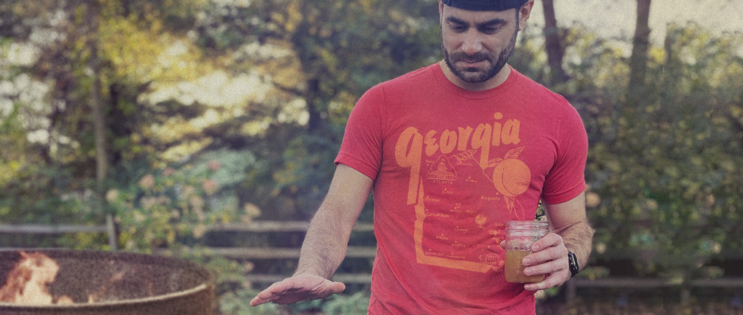 Man in a red 'Georgia' t-shirt holding a jar outdoors with greenery in the background