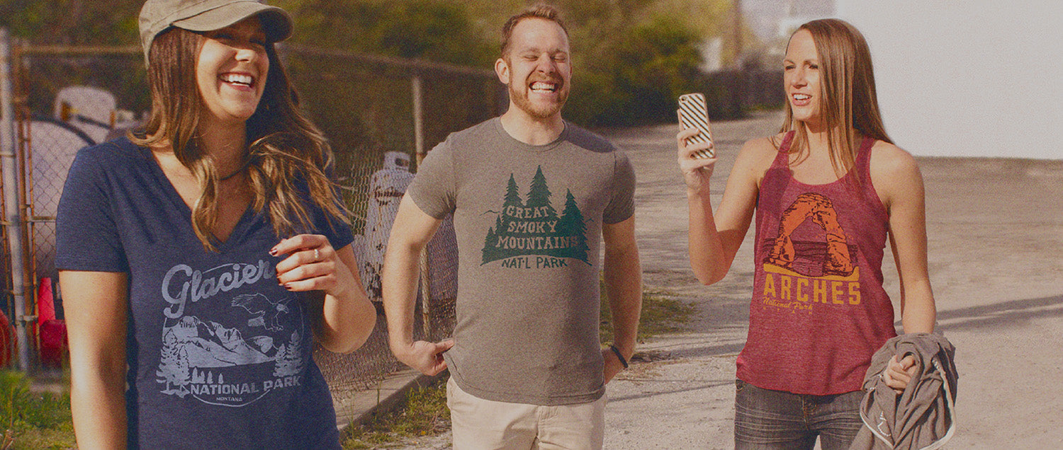 Three people standing outdoors, wearing t-shirts with nature-themed designs.