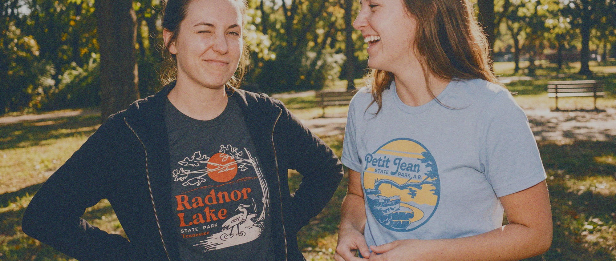 Two people standing outdoors in a park, wearing t-shirts with visible designs.